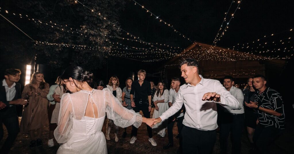 Mariés et invités dansant sous les guirlandes lumineuses pendant la soirée de mariage